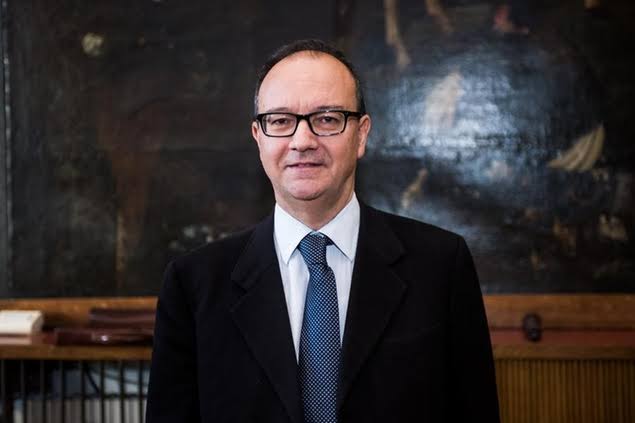 Giuseppe Valditara in a dark suit standing in front of a large classical painting