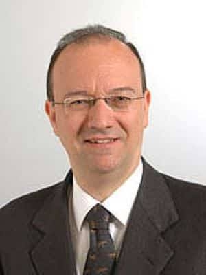 Earlier portrait of Giuseppe Valditara smiling, in a grey jacket and patterned tie against a white background