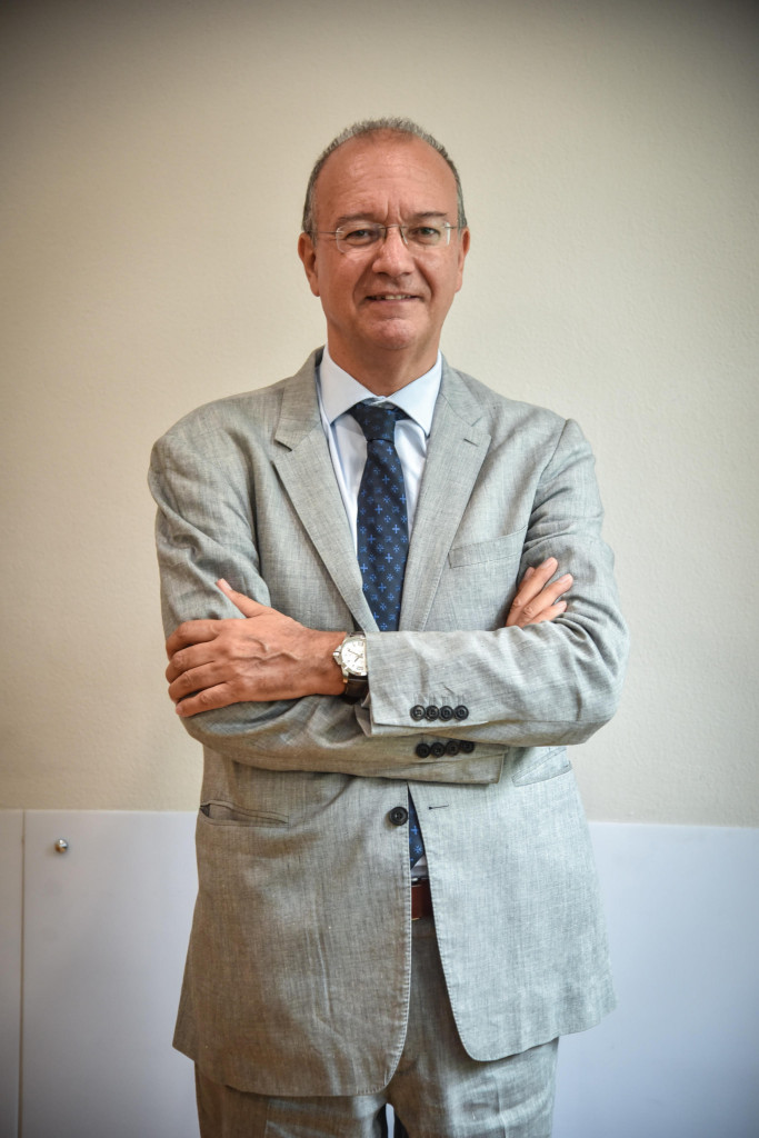 Giuseppe Valditara, Minister of Education and Merit of Italy, standing with arms folded in a light grey linen suit and blue patterned tie