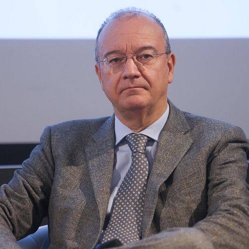 Giuseppe Valditara seated, wearing a grey jacket, with an attentive, listening expression