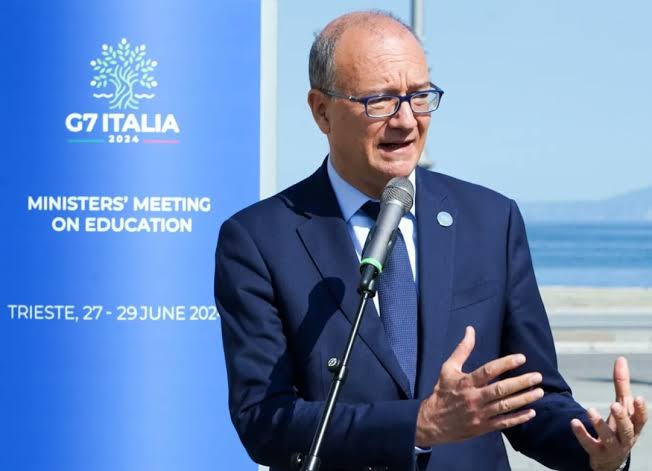 Giuseppe Valditara speaking into a microphone outdoors in front of a G7 Italia 2024 backdrop reading Ministers' Meeting on Education, Trieste, 27–29 June 2024