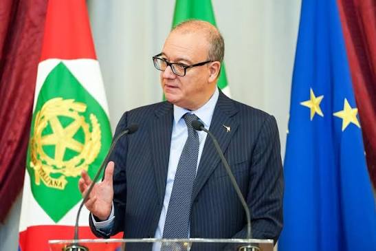 Giuseppe Valditara speaking at a lectern beside the emblem of the Italian Republic, with the flag of the European Union behind him