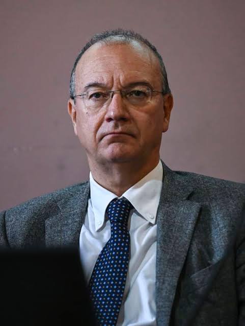 Standing portrait of Giuseppe Valditara wearing a grey jacket, white shirt and dotted tie against a neutral backdrop